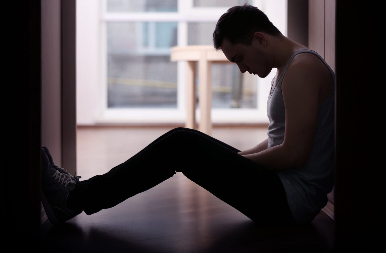 A man sitting on the ground in front of a window.